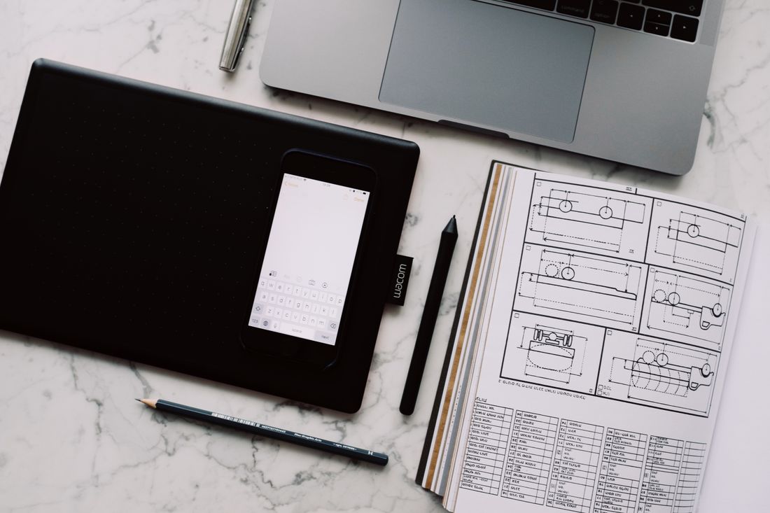 Drawing tablet, laptop and design papers on a marble desk.